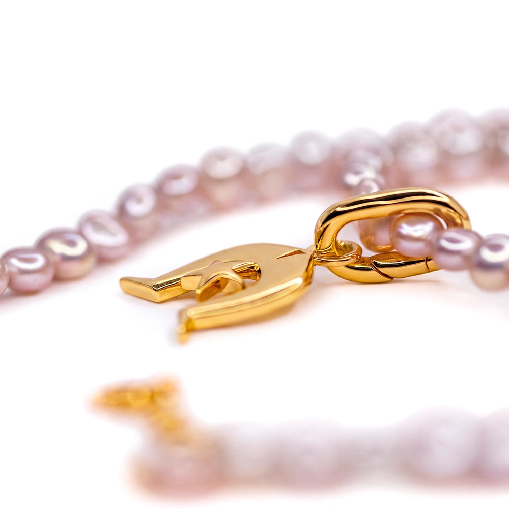 A close-up of a gold Dhoeri Headdress Pendant from the Torres Strait Islands featuring light pink freshwater pearls and a polished gold lobster clasp on a white background.