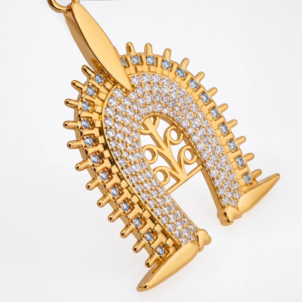 Torres Strait Island Gold-plated Dhoeri Headdress pendant necklace adorned with pave-set clear stones and small blue accent stones, suspended from a gold chain on a white background with a soft reflection.