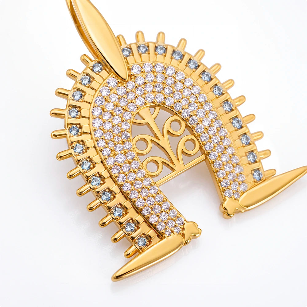 Torres Strait Island Gold-plated Dhoeri Headdress pendant necklace adorned with pave-set clear stones and small blue accent stones, suspended from a gold chain on a white background with a soft reflection.